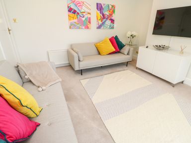A living room with two sofas colorful cushions abstract paintings a rug and a television on a cabinet at Robin Hill in Duporth near St Austell