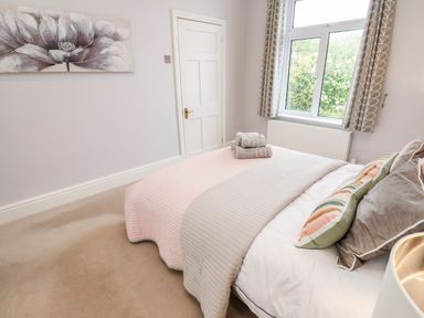 A bedroom with a bed covered by a pink and gray blanket and folded towels on top at Robin Hill in Duporth near St Austell