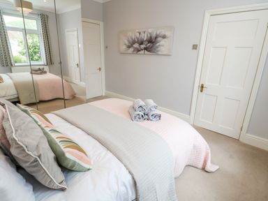 A bedroom with a bed covered in gray and pink bedding with rolled towels placed on top and a mirrored wardrobe on one side at Robin Hill in Duporth near St Austell