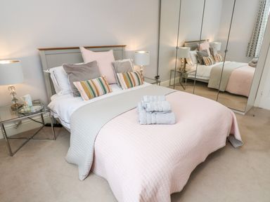 A bedroom with a double bed pillows bedside tables lamps mirrored wardrobes at Robin Hill in Duporth near St Austell