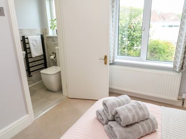 A bedroom with folded towels on a bed next to an open door leading to a bathroom with a toilet and towel rack at Robin Hill in Duporth near St Austell