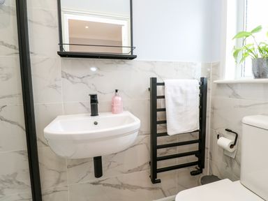 A bathroom with a wall-mounted sink with black faucet a towel rack a toilet and a window with a plant at Robin Hill in Duporth near St Austell