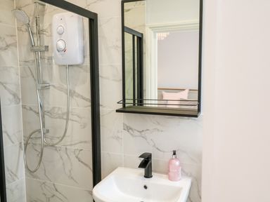 A bathroom with a shower, a sink with a black faucet, a mirror, and a soap dispenser at Robin Hill in Duporth near St Austell