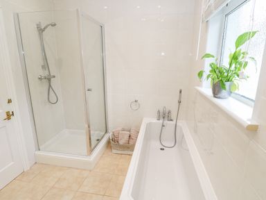 A bathroom with a shower enclosure a bathtub a basket with towels and a plant on the windowsill at Robin Hill in Duporth near St Austell