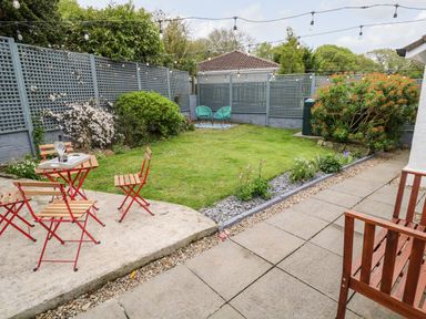 A garden with a small table and chairs on a concrete patio and two blue chairs on a grass lawn at Robin Hill in Duporth near St Austell