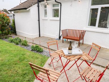 An outdoor patio with a wooden table and four wooden chairs with red frames and a wooden bench near a white house at Robin Hill in Duporth near St Austell
