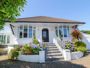 A front view of a white house with steps leading to a wooden door and flower beds on either side at Robin Hill in Duporth near St Austell
