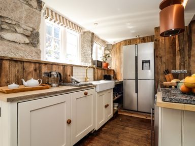 A kitchen with wooden cabinets a silver refrigerator a sink and wooden walls at Roncon's Villa in Goldsithney