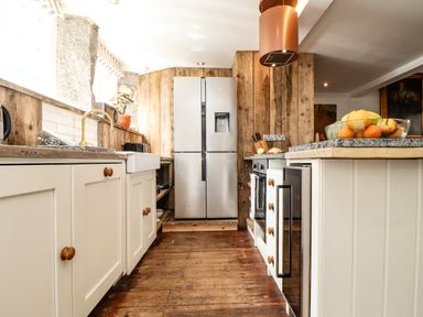 A kitchen with wooden floors white cabinets a refrigerator and a fruit bowl on the counter at Roncon's Villa in Goldsithney