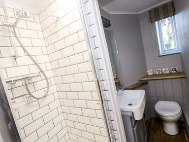 A bathroom with a shower with white tiled walls a toilet and a sink with a mirror and a small window at Roncon's Villa in Goldsithney