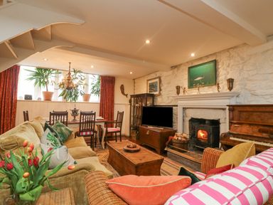 A living room with sofas a fireplace a wooden chest a dining table with chairs plants and a piano at Roncon's Villa in Goldsithney