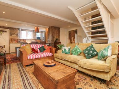 A living room with two sofas and a wooden chest coffee table under white stairs at Roncon's Villa in Goldsithney