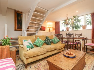 A living room with a mustard sofa and green pillows a wooden coffee table and a dining table with chairs at Roncon's Villa in Goldsithney