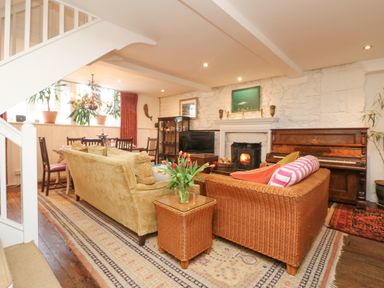 A living area with a fireplace, a piano, sofas, a dining table, and plants at Roncon's Villa in Goldsithney