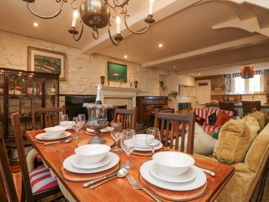 A dining area with table set for six and a living area with sofas and a piano at Roncon's Villa in Goldsithney