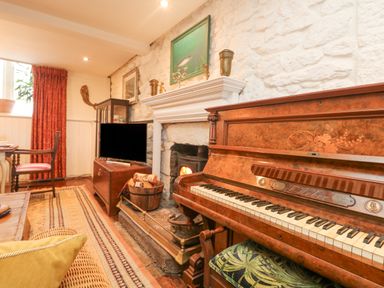 A living room with a piano near a stone fireplace and a television at Roncon's Villa in Goldsithney