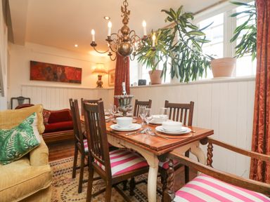 A dining area with a wooden table set with plates glasses and cutlery surrounded by chairs with pink and white striped cushions at Roncon's Villa in Goldsithney