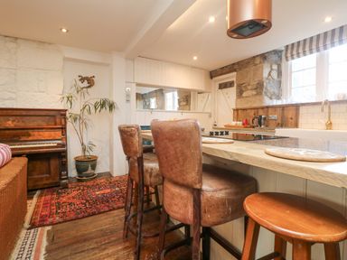 A kitchen with a wooden counter and bar stools a piano a plant and a rug at Roncon's Villa in Goldsithney