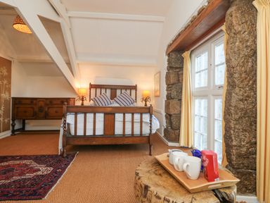 A bedroom with a wooden bed frame two bedside lamps a wooden sideboard and a tray with mugs on a wooden stump near a window at Roncon's Villa in Goldsithney