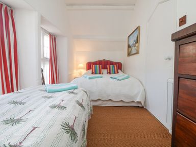 A bedroom with two beds red striped curtains and a wooden dresser at Roncon's Villa in Goldsithney
