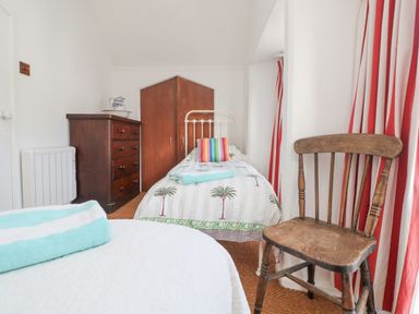 A bedroom with two single beds a wooden chair a chest of drawers and striped curtains at Roncon's Villa in Goldsithney