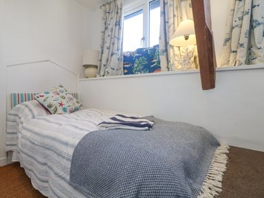 A bedroom with a single bed striped bedding decorative pillows a window with curtains and two lamps at Roncon's Villa in Goldsithney