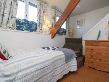 A bedroom with a bed a wooden dresser carpeted stairs and windows with patterned curtains at Roncon's Villa in Goldsithney