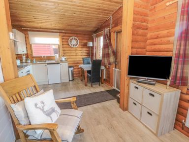 A wooden room with a rocking chair a kitchen area a dining table with chairs and a TV on a cabinet at Ingram in Longframlington