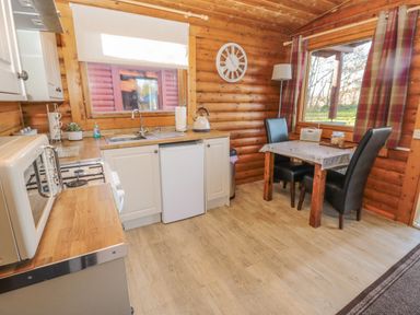 A kitchen with wooden countertops a microwave a stove a sink and a small dining table with two black chairs at Ingram Longframlington