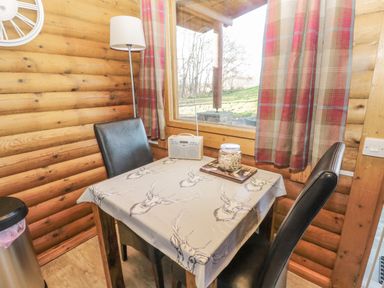 A small dining area with a table covered by a deer print tablecloth two black chairs a window with plaid curtains and a wooden wall at Ingram in Longframlington