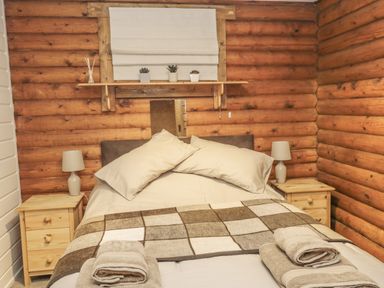 A bedroom with a double bed two bedside tables lamps and wooden log walls at Ingram in Longframlington