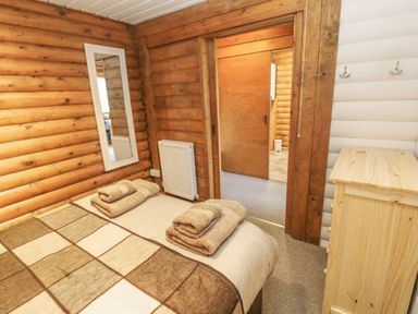A bedroom with a bed covered in a patchwork blanket and folded towels by a wooden dresser and a wall mirror at Ingram Longframlington
