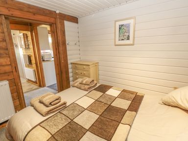 A bedroom with a bed covered in a brown checkered blanket with folded towels on it a small wooden chest of drawers a map on the wall and a view into a bathroom at Ingram in Longframlington