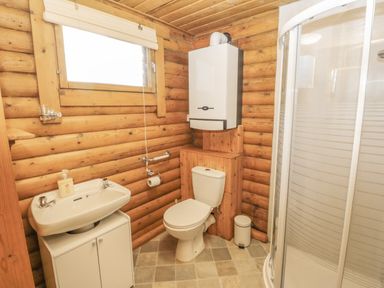 A bathroom with a sink cabinet toilet shower cubicle and water heater on wooden log walls at Ingram Longframlington