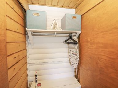 A small wooden closet with an ironing board hangers an iron and storage boxes at Ingram in Longframlington