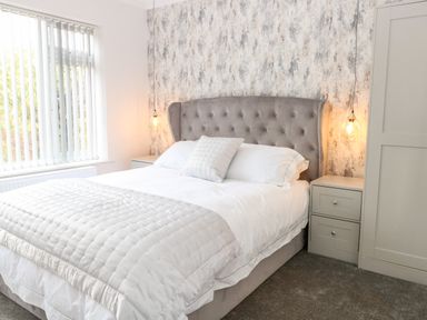 A bedroom with a bed a bedside table a lamp and a window with vertical blinds at Harbour Place in Wells-Next-The-Sea