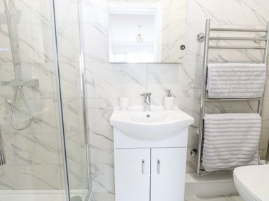 A bathroom with a sink cabinet a mirror a glass shower enclosure and a towel rack with towels at Harbour Place in Wells-Next-The-Sea