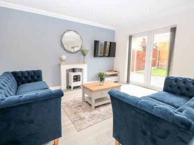 A living room with blue sofas a coffee table a TV mounted on a wall and patio doors at Harbour Place in Wells-Next-The-Sea