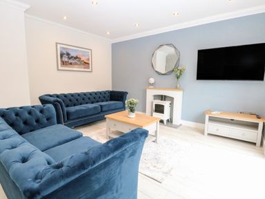 A living room with blue sofas a wooden coffee table a mirror above a fireplace and a wall mounted television at Harbour Place in Wells-Next-The-Sea