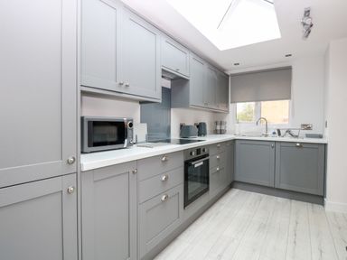 A kitchen with grey cabinets and drawers a microwave an oven a toaster and a window with a blind at Harbour Place in Wells-Next-The-Sea