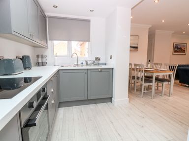 A kitchen with grey cabinets and white countertops next to a dining area with a table and four chairs at Harbour Place in Wells-Next-The-Sea