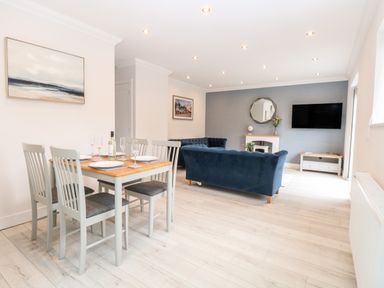 A dining area with a table set for four and a living room with blue sofas and a mounted television at Harbour Place in Wells-Next-The-Sea