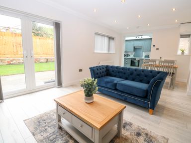 A living area with a blue sofa a wooden coffee table and dining table near a kitchen at Harbour Place in Wells-Next-The-Sea