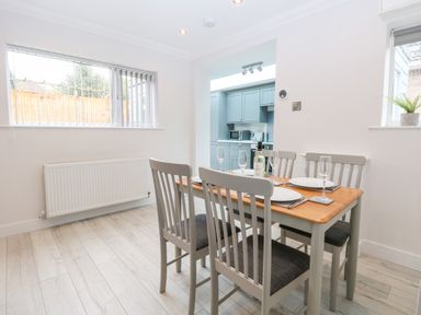 A dining area with a wooden table and four chairs set with plates and glasses next to a kitchen at Harbour Place in Wells-Next-The-Sea