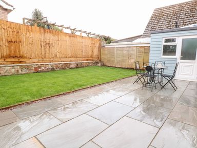 A backyard with a wet tiled patio a metal table with four chairs a lawn and wooden fences at Harbour Place in Wells-Next-The-Sea