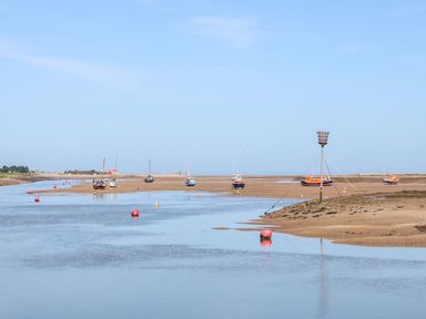 A river with anchored boats and buoys on a sandy shore at Harbour Place in Wells-Next-The-Sea