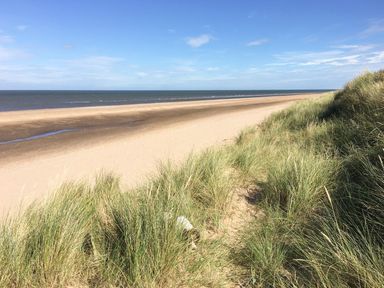 A sandy beach with ocean waves and tall grass dunes at Harbour Place in Wells-Next-The-Sea