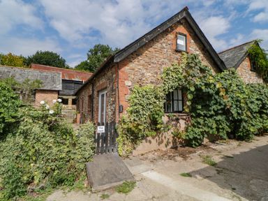 Stone cottage covered with climbing plants and a wooden gate with the name The Holt in Harcombe near Sidford