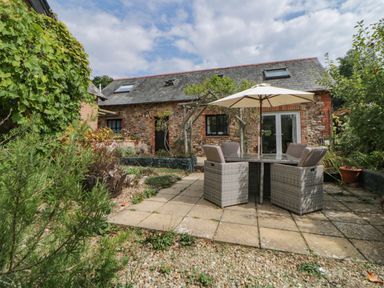A stone house with slate roof and skylights with a patio table chairs and umbrella in the garden at The Holt Harcombe near Sidford
