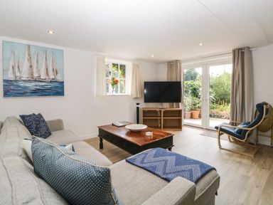 A living room with a gray sofa blue cushions wooden coffee table flat screen TV and a chair near patio doors at The Holt in Harcombe near Sidford